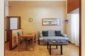 Una sala de estar con un sofá, una mesa, una silla, un cuadro y una lámpara.