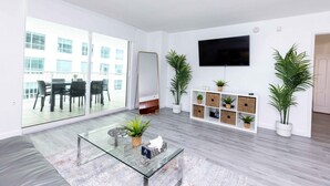A modern living room with a glass coffee table, a flat-screen TV mounted on the wall, and a large sliding glass door leading to an outdoor balcony. - Luxury Huge APT@Brickell, Free Parking. (Miami)