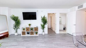 A modern living room with a flat-screen TV, a white console table with potted plants, and a clear glass chair. - Luxury Huge APT@Brickell, Free Parking. (Miami)