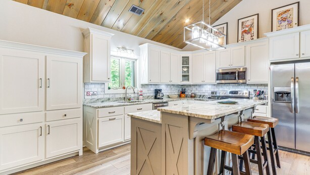 A modern kitchen with white cabinets, a central island with bar stools, stainless steel appliances, and a wooden ceiling. - Deck, Fire Pit & Fireplace: Murphy Forest Retreat (Murphy)
