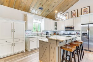 A modern kitchen with white cabinets, a central island with bar stools, stainless steel appliances, and a wooden ceiling. - Deck, Fire Pit & Fireplace: Murphy Forest Retreat (Murphy)