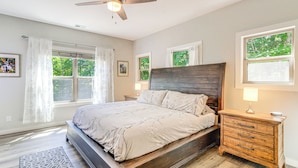 A bedroom with a bed, a nightstand, a dresser, a ceiling fan, and windows with curtains. - Deck, Fire Pit & Fireplace: Murphy Forest Retreat (Murphy)