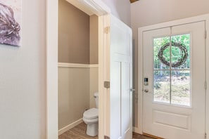 A bathroom with a toilet, a door with a wreath, and a window with a view of greenery. - Hike, Fish & Kayak: Murphy Gem w/ Deck & Fire Pit (Murphy)