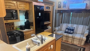 A compact RV kitchen with a stove, sink, and refrigerator, a small dining area, and a living space with a couch and curtains. - North Georgia Mountain Getaway (Cleveland)
