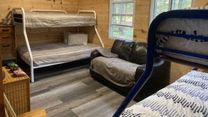 A wooden cabin room with bunk beds, a leather sofa, a dresser, and a window with a view of trees. - Clear water and breath taking view! (Trent Lakes)
