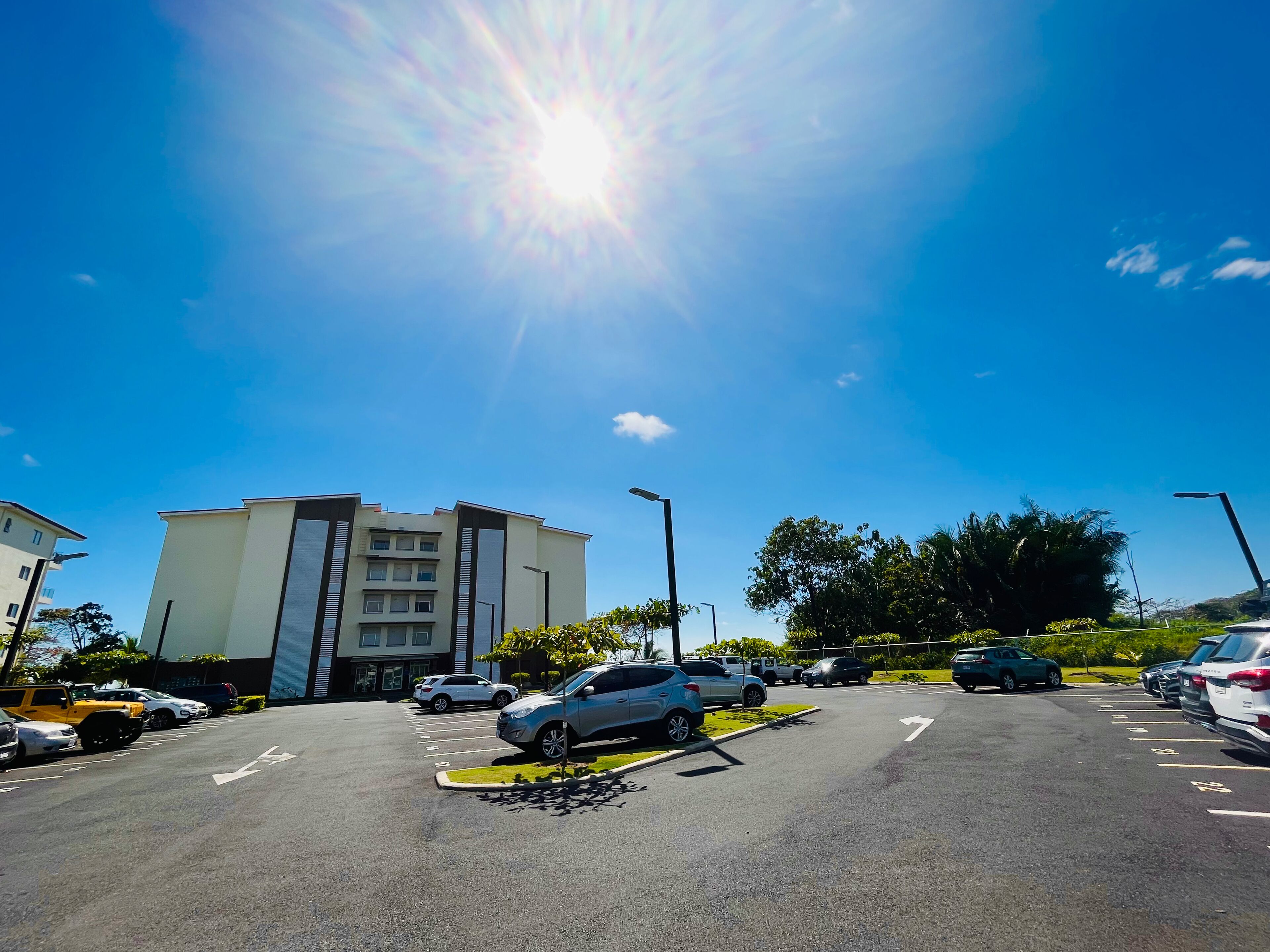 A parking lot with multiple cars, a building with a modern design, and a clear blue sky.