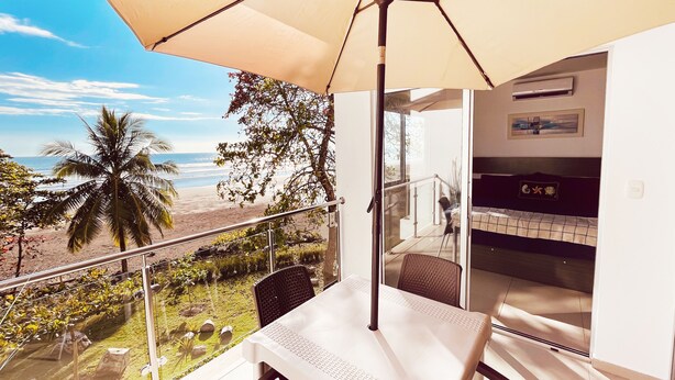 Een balkon met een tafel en stoelen, uitzicht op het strand en een palmboom.