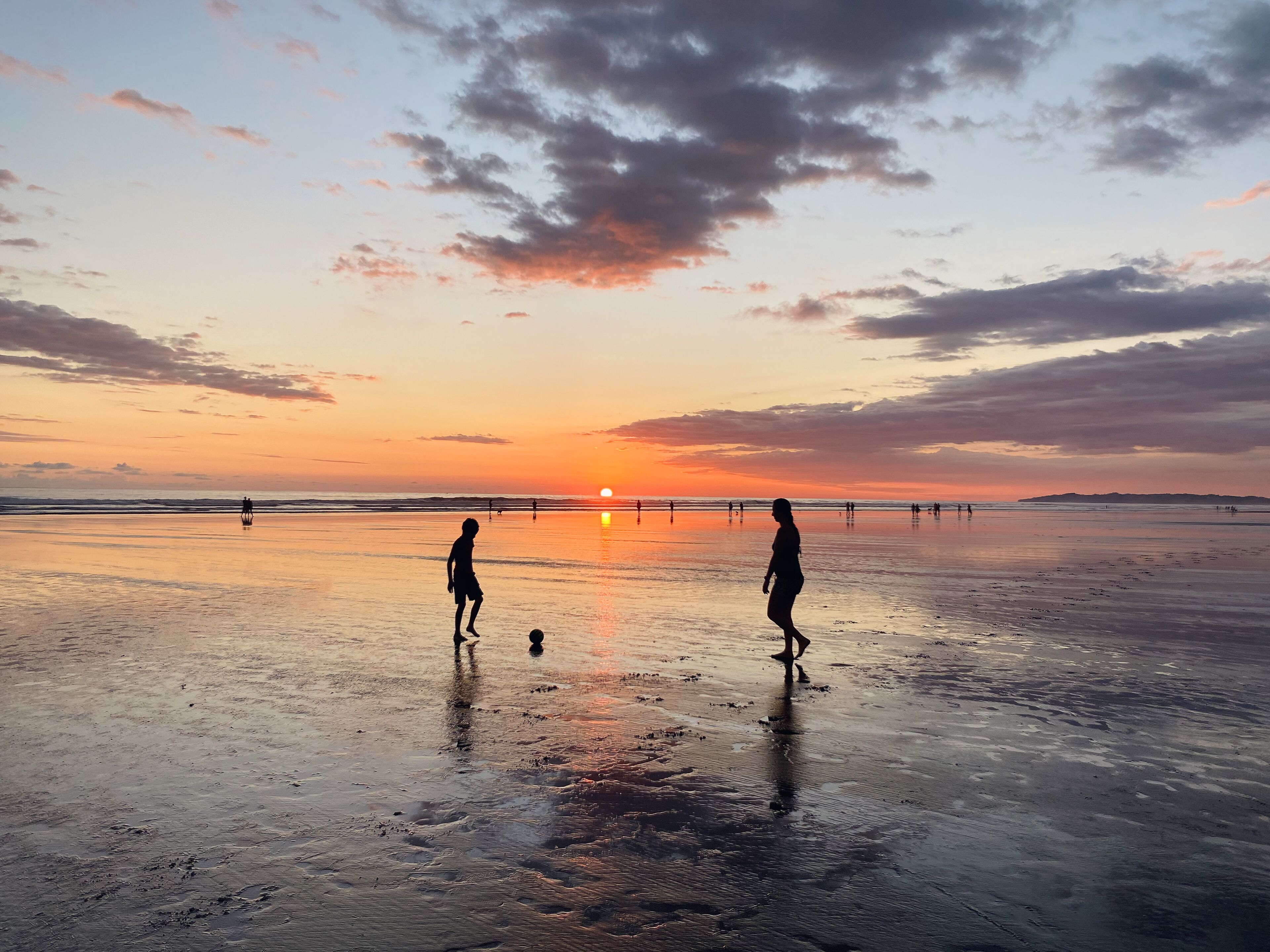 A beach at sunset with people walking and playing.