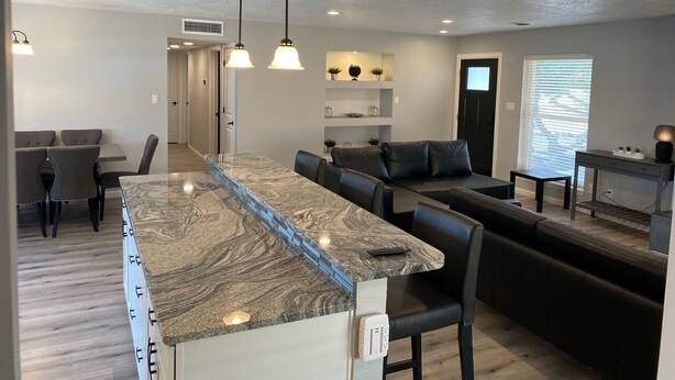 A modern kitchen with a marble countertop, black leather seating, pendant lighting, and a built-in island.