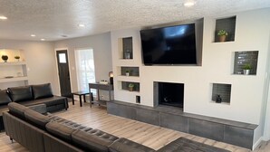 A modern living room with a large sectional sofa, a flat-screen TV mounted on the wall, and a fireplace.