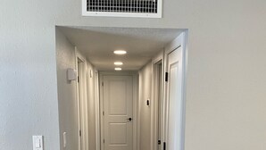 A hallway with a wooden floor, white walls, and a ceiling vent.
