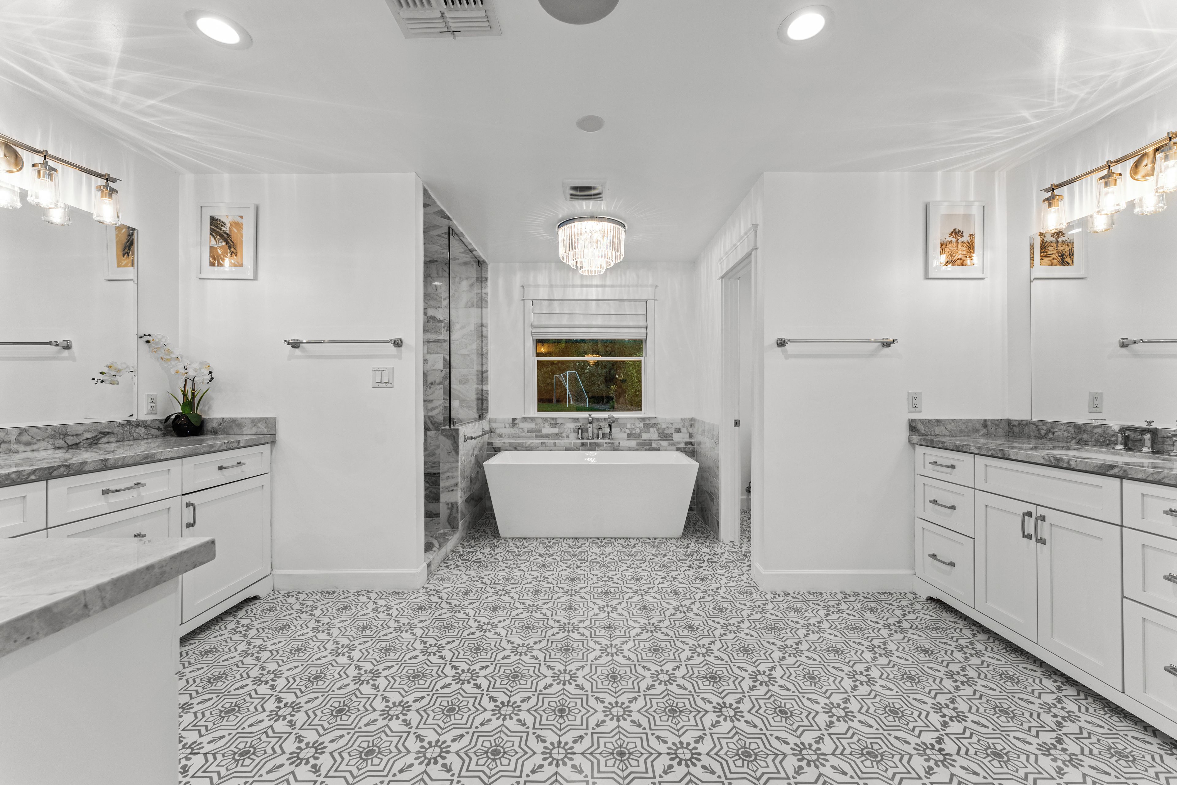 Un baño moderno con una bañera independiente, muebles blancos y baldosas de suelo con diseño.