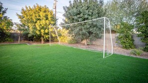 Ein gepflegter Garten mit einem Fußballtor, einem ordentlich gestutzten Rasen und verschiedenen Bäumen und Sträuchern.