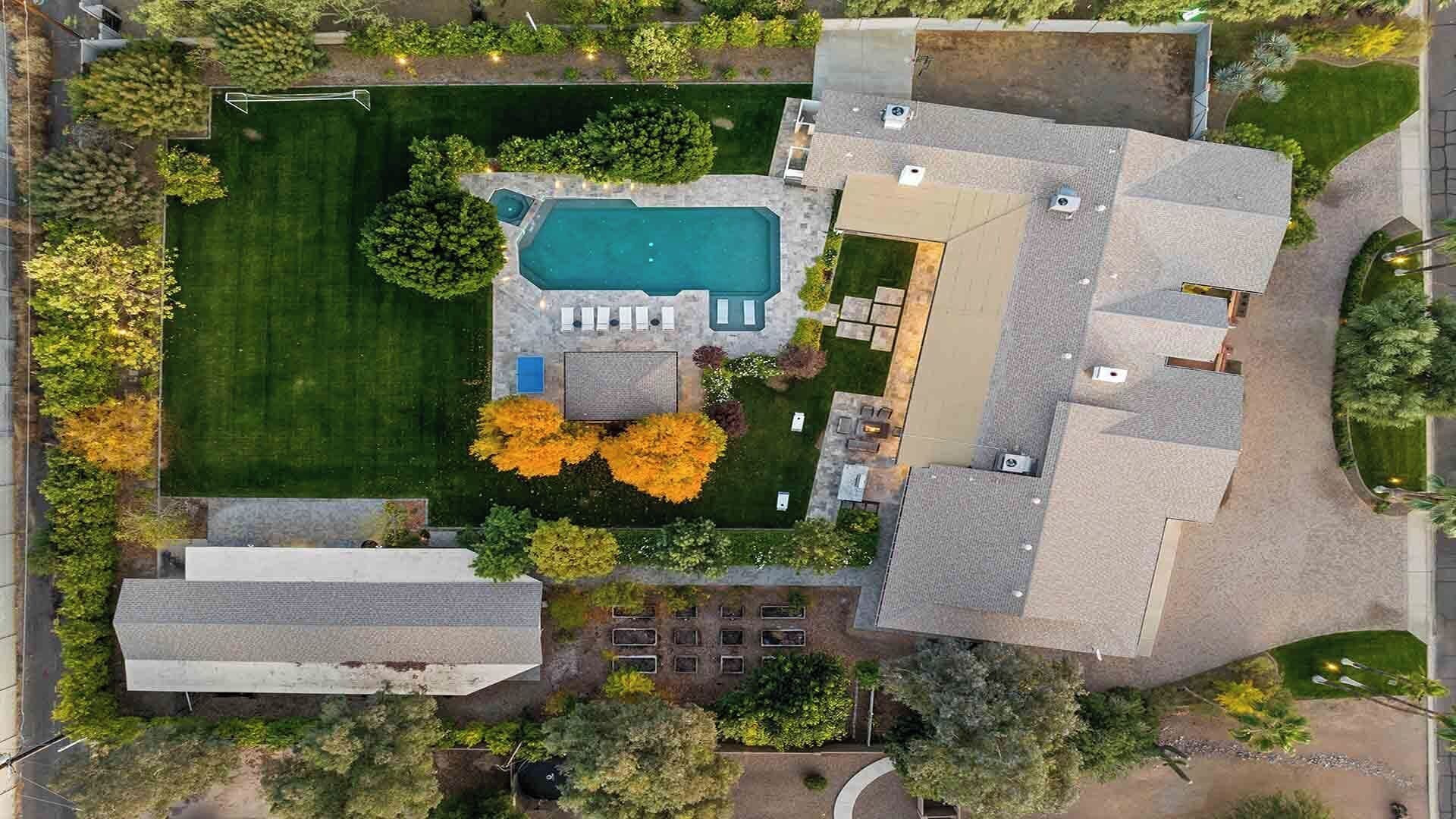 An aerial view of a residential property with a swimming pool, a patio area, and a large house with a sloped roof.