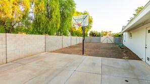 Ein Garten mit Basketballkorb, einer Ziegelmauer und einer Betonplatte.