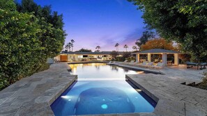 Ein Schwimmbecken mit modernem Design, umgeben von einem angelegten Garten und einer überdachten Terrasse.