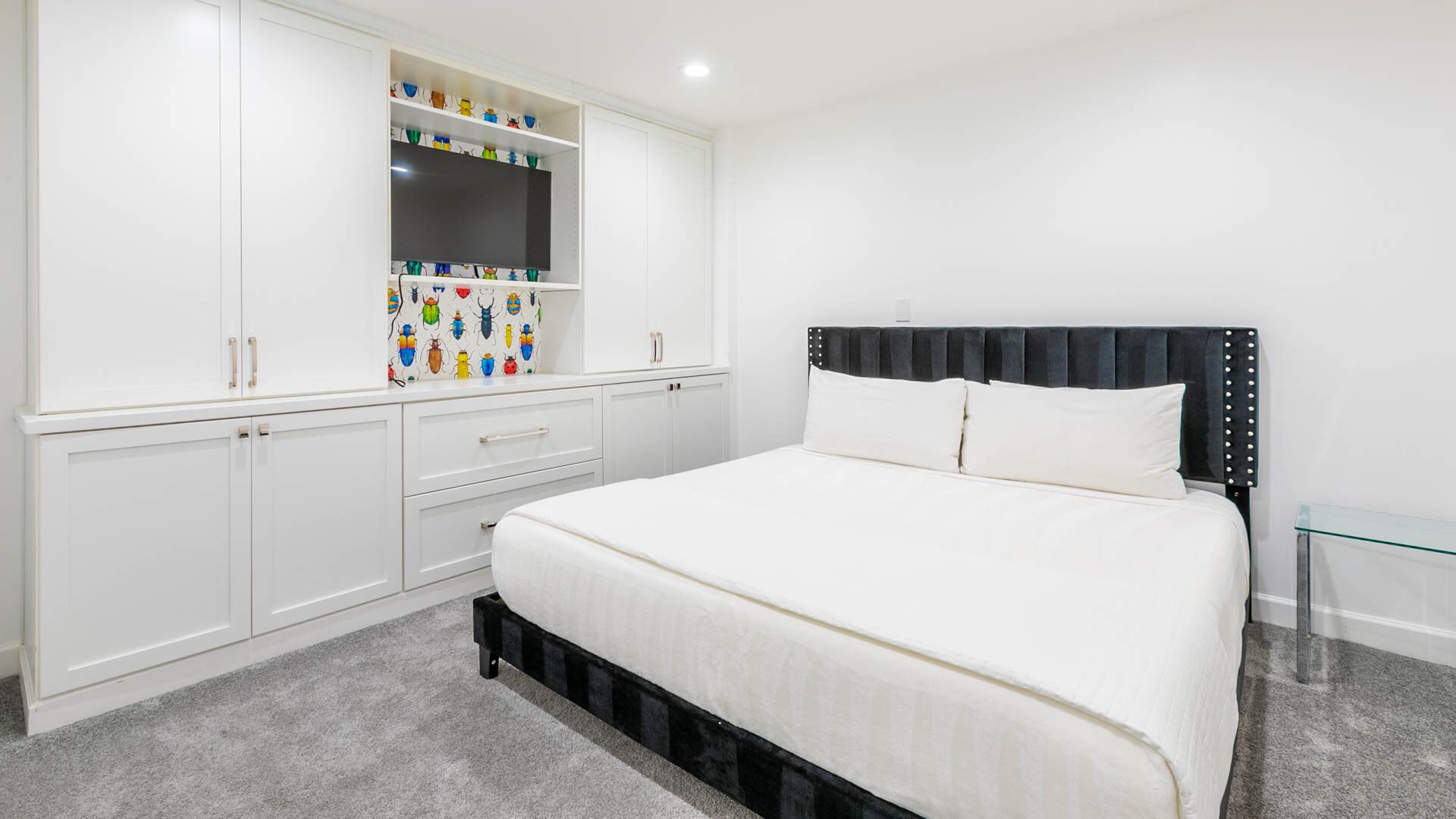 Un dormitorio con cama, armario blanco y estante con objetos de colores.