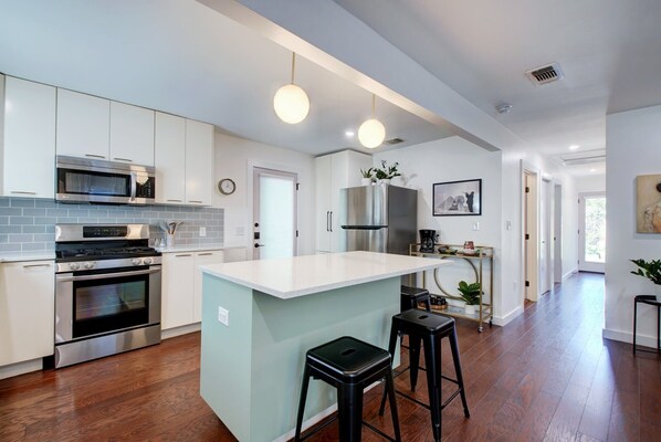 Una cocina moderna con armarios blancos, electrodomésticos de acero inoxidable y una isla central con taburetes.