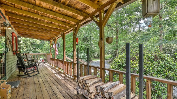 A wooden deck with a railing, a rocking chair, and a pile of firewood. - Rustic Cabin trout fishing dog loving beach area on secluded 8 acres! HL# 001504 (Ellijay)