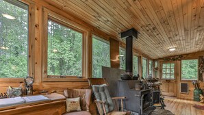 A cabin interior with large windows, a fireplace, wooden furniture, and a rustic stone floor. - Rustic Cabin trout fishing dog loving beach area on secluded 8 acres! HL# 001504 (Ellijay)