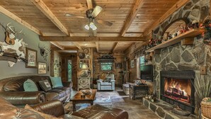 A rustic cabin interior with a stone fireplace, leather furniture, and a ceiling fan. - Rustic Cabin trout fishing dog loving beach area on secluded 8 acres! HL# 001504 (Ellijay)