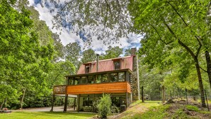 A modern two-story house with a wooden deck and large windows, surrounded by lush greenery. - Rustic Cabin trout fishing dog loving beach area on secluded 8 acres! HL# 001504 (Ellijay)