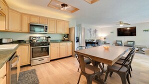 Een moderne keuken met houten kasten, roestvrijstalen apparatuur, een eethoek met een houten tafel en stoelen, en een plafondventilator.