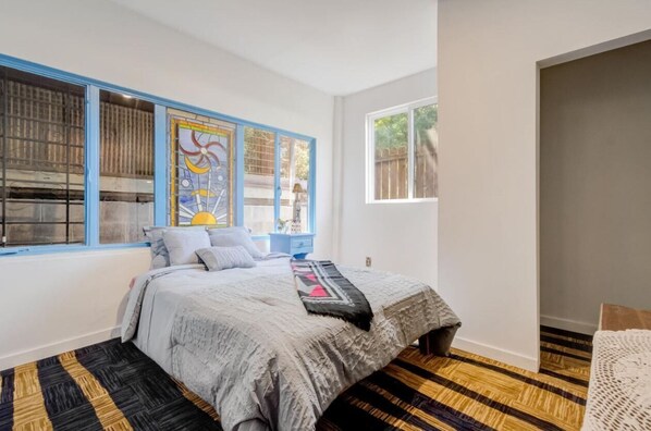 A bedroom with a bed, a window with blue shutters, a wooden floor, and a view of the outside. - Relax in an unique artistic house and with nature (Oakland)