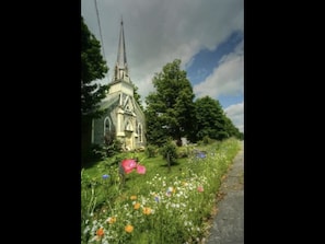 Stroll through the serene landscape surrounding this traditional church, surrounded by vibrant wildflowers and a picturesque steeple.