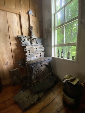 Enjoy a warm, traditional atmosphere in this room, featuring a rustic fireplace and a large window with a view of lush greenery.