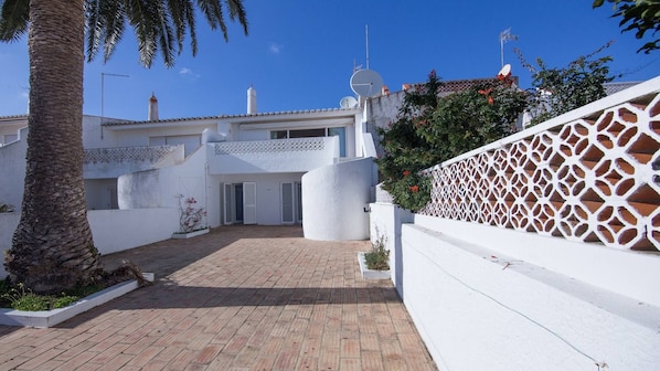 A courtyard with a paved walkway, white walls, and a palm tree.