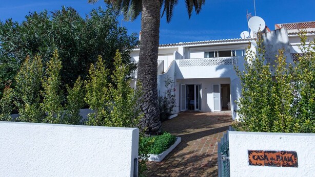 A white building with a paved entrance, surrounded by greenery and a clear blue sky.