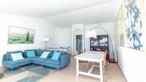 A modern living room with a sectional sofa, a dining table with chairs, a floor lamp, and artwork on the walls.