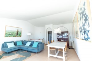 A modern living room with a sectional sofa, a dining table with chairs, a floor lamp, and artwork on the walls.