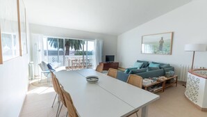 A modern living room with a white sofa, a dining table, and a balcony with a view.