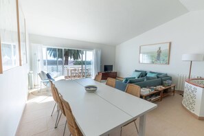 A modern living room with a white sofa, a dining table, and a balcony with a view.