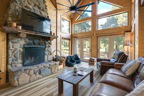 A cozy cabin interior with a stone fireplace, leather sofa, and large windows. - Spacious & Quiet Pagosa Springs Cabin w/ Deck! (Pagosa Springs)