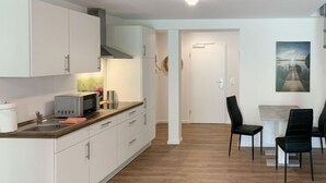 A modern kitchen with white cabinets, a microwave, and a sink. There is a dining area with a table and chairs. - Langeoog by Interhome (Westerholt)