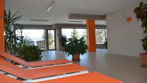 Un espace intérieur spacieux, agrémenté de fauteuils orange, de plantes en pot et de grandes fenêtres qui laissent entrer la lumière naturelle.