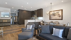 A modern living room with a gray sofa, ottoman, and a dining area with a table set for two. - Walk to the ski slopes, restaurants & shops.  Location is everything! (Steamboat Springs)