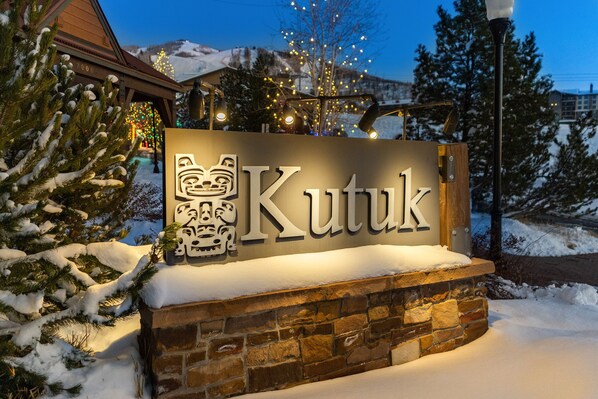A sign with the name 'Kutuk' in a stylized font, set against a stone wall with snow accumulation.