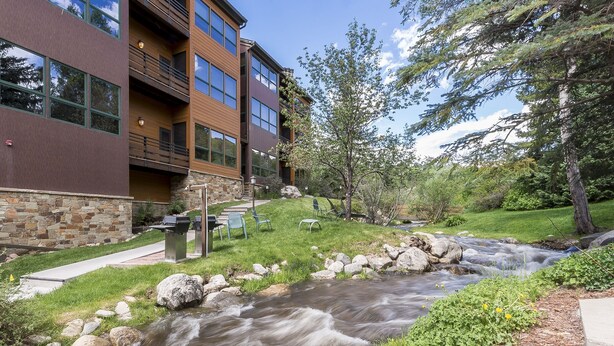 A modern building with a stone facade, a balcony, and a small stream flowing in front. - Walk to the ski slopes, restaurants & shops.  Location is everything! (Steamboat Springs)