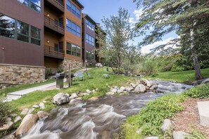 A building with a stone facade, a grassy area, and a flowing stream.