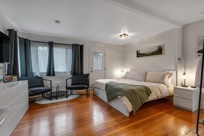 Ein modernes Schlafzimmer mit Holzboden, einem Bett mit weißer Bettwäsche, einem Schreibtisch mit Stuhl und einem Fenster mit Vorhängen.
