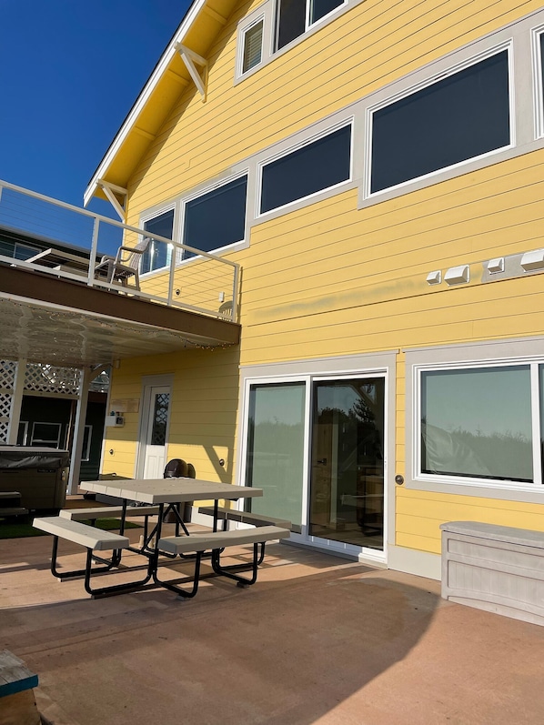 A two-story yellow building with a covered patio area featuring picnic tables and a barbecue grill.