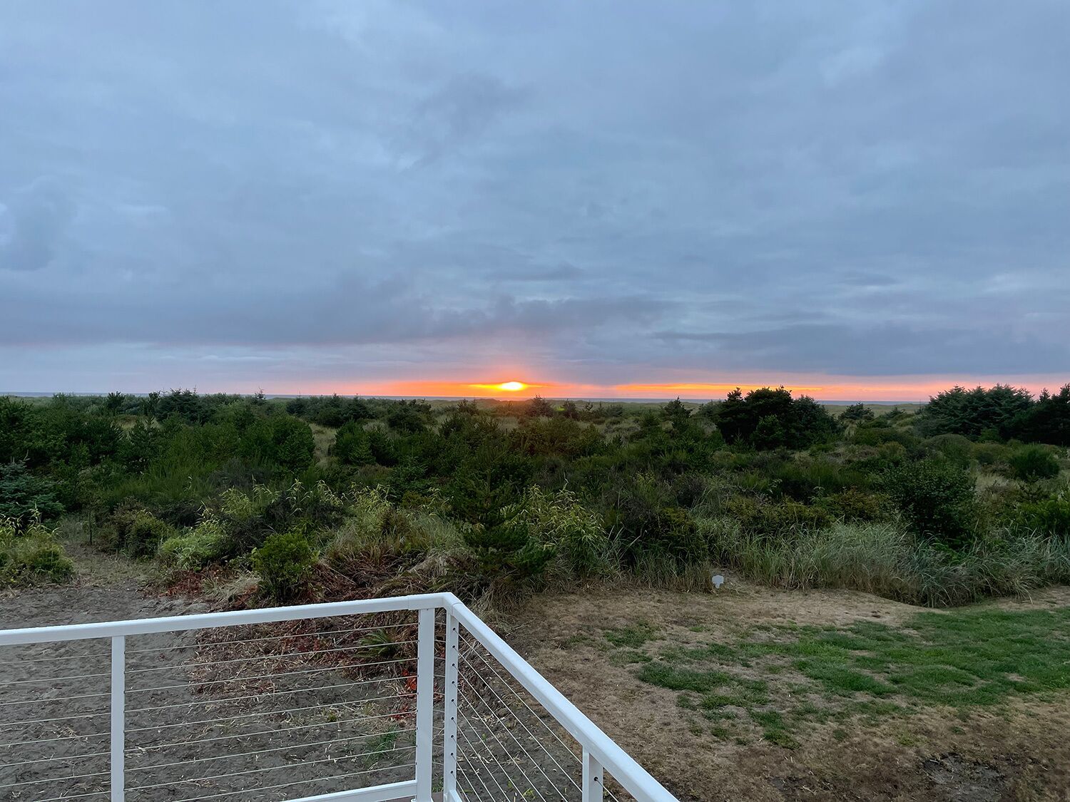 Ein Sonnenuntergang über einer natürlichen Landschaft mit einer weißen Metallreling im Vordergrund.