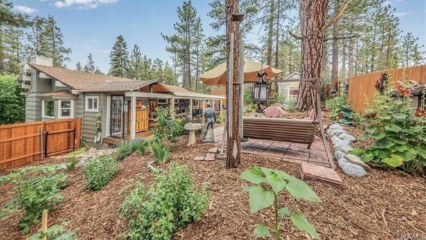 A residential property with a house, garden, and forested backdrop. - Gorgeous cabin great for Family & Pets BBQ fenced backyard fire pit Jacuuzi (Big Bear City)