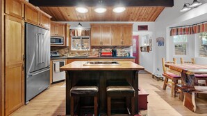 A kitchen with wooden cabinets, a stainless steel refrigerator, a microwave, and a wooden island with stools. - Gorgeous cabin great for Family & Pets BBQ fenced backyard fire pit Jacuuzi (Big Bear City)
