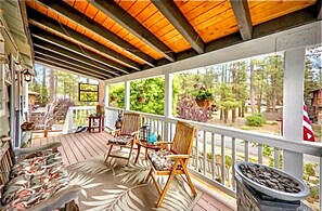 A covered porch with wooden chairs and a table, surrounded by potted plants and a fire pit.