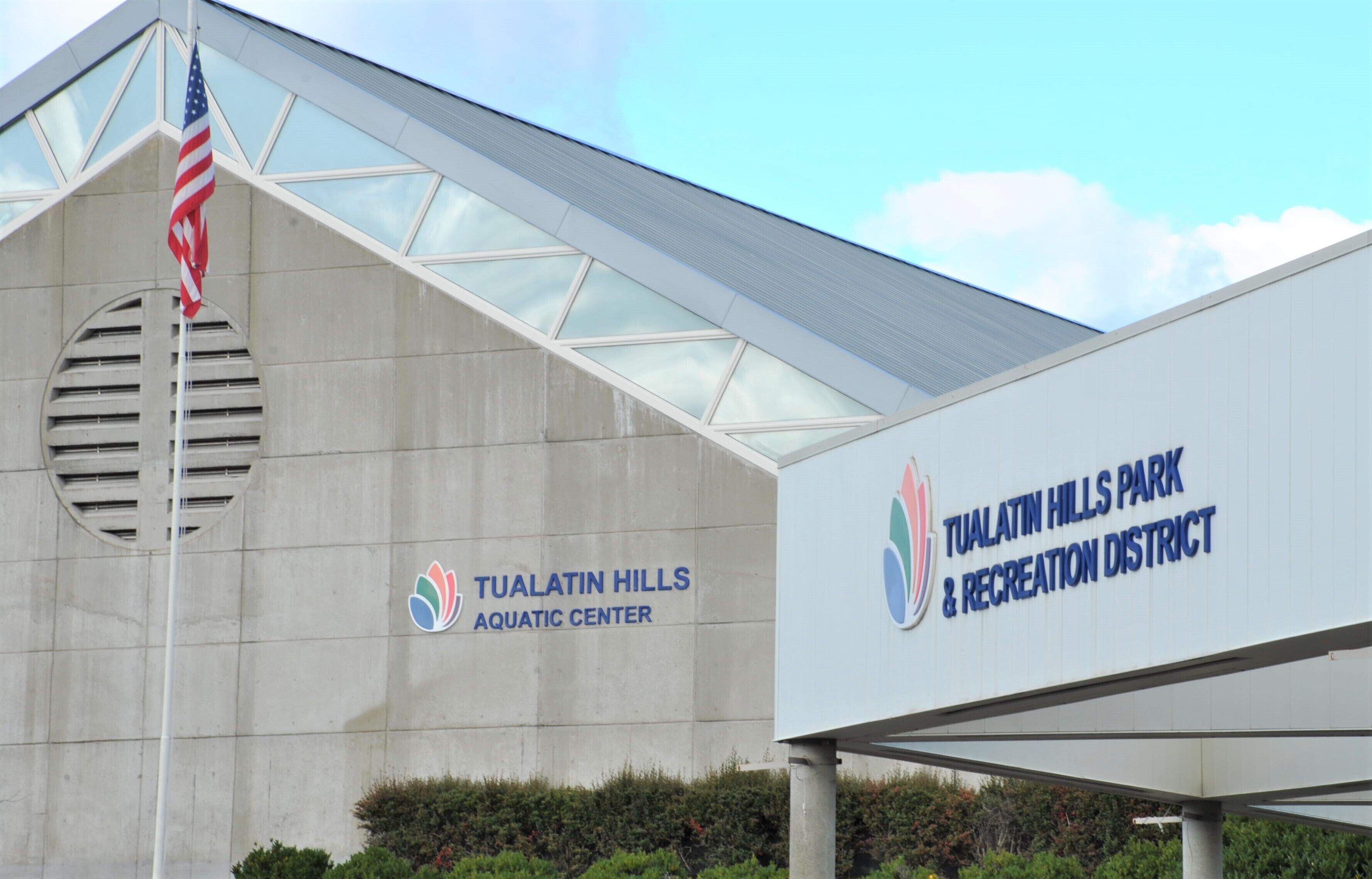 The Tualatin Hills Park & Recreation District Aquatic Center building with a large sign, an American flag, and a clear sky.